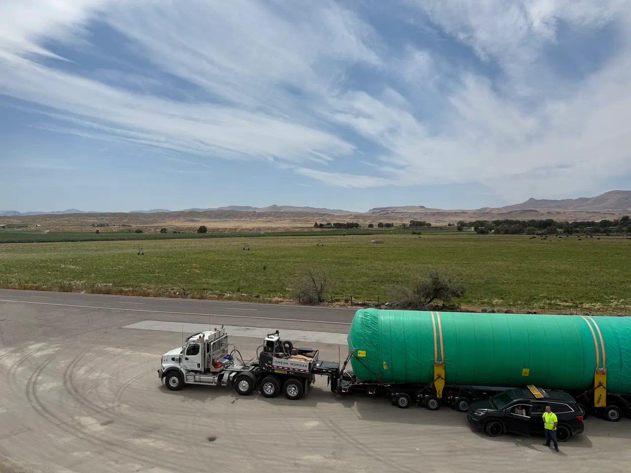 Green-wrapped industrial load and escort vehicle staged beside a rural highway